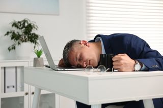 Man with cup of drink sleeping at table in office