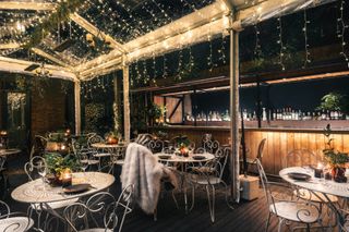 chairs and tables with fur blankets on a terrace, under fair lights and a clear roof