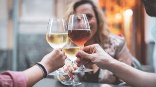 Three people drinking alcohol from stemmed glasses