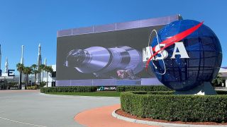 a large blue sphere with the word "NASA" on it in front of a large LED screen showing a rocket in flight
