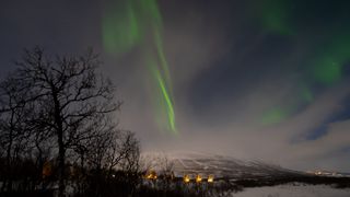 northern lights appear through the clouds above Abisko, Sweden. 