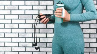 Person holding a water bottle in left hand and one of the best weighted jump ropes in right hand against brick wall