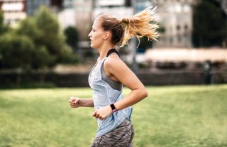 A woman wearing a fitness tracker while running in an park outdoors.