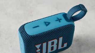 A photo of the JBL Go 4 in blue on a concrete surface against a blue wall.