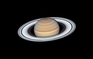 Saturn, a dusty brown orange planet has a striking series of rings closely packed in together, encircling the planet. The rings appear white/gray in color.