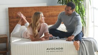 A couple sit and laugh on the Avocado Eco Organic Mattress