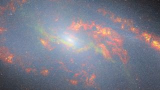 A dusty-looking section of space with orange and red streaks concentrated around a glowing greenish center.