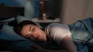 A woman sleeping on her front looking towards the camera in bed looking tired from not sleeping