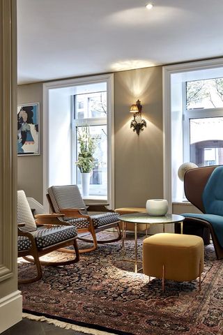 A sitting area with two rocking chairs, a wing back chair, a round coffee table and a patterned rug next to two large windows.