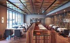 Restaurant with tables, chairs, wooden counter and glass windows.