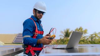 Man in high vis ropes checking solar panel on a laptop