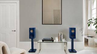 A pair of stand-mounted KEF R3 Meta in indigo gloss special edition flanking a glass coffee table in a white room.