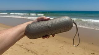 Beats Pill Bluetooth speaker held in hand with beach and sea in background