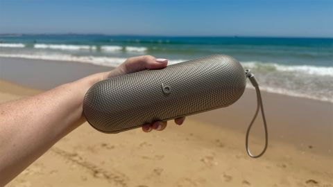 Beats Pill Bluetooth speaker held in hand with beach and sea in background