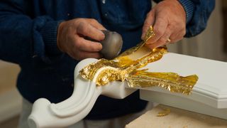 An artisan applies a gold leaf to wood by using the "guazzo" technique, burnishing the gold leaf with an agate, in a workshop of Florence.