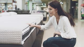 A woman with long dark hair feels the firmness of a mattress she is looking at