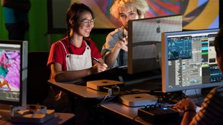 People sit in front of a set of Apple monitors. They are using Mac mini computers and a digital drawing tablet.