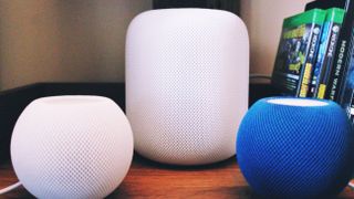 A white Homepod alongside two homepod minis, one white one blue