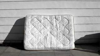 An old white patterened mattress propped against a wall outside