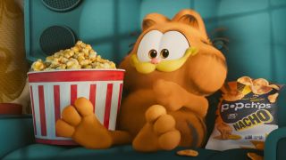 Garfield sits in a chair with a tub of popcorn in The Garfield Movie. 