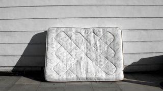 An old mattress leans against the side of a building