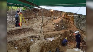 Researchers inspect the former cave entrance at Einhornhöhle, where they found the carved giant deer toe. The artifact was found about 3 feet (1 meter) behind the individual holding the staff.