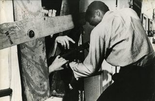 A man sticks a gun through a boarded up window while hands reach inside in Night of the Living Dead (1968)