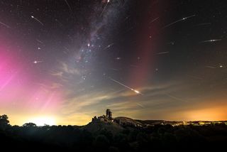 a view of the night sky with an old castle ruin in the foreground. There is a pink hue on the left which is the northern lights and lots of streaks of light which are the perseid meteor and toward the center right of the image is a long red glow which is known as a SAR arc. 