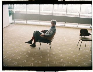 Chair by Robin Day photographed on a patterned carpet with the designer's daughter Paula Day sitting on the chair