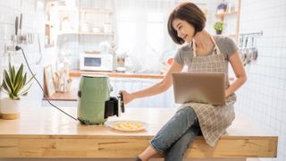 A woman opening an air fryer in a kitchen