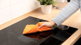 Woman cleaning an induction cooktop with an ornage cloth