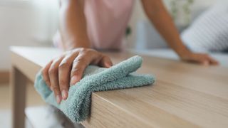 A green microfiber cloth being used to clean a wooden surface