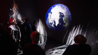 NASA experts stand in a dark room with Earth visualizations to show the impacts of climate change.