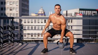 Man outside on balcony squatting with a kettlebell in left hand