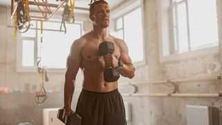 Man holding two dumbbells and raising one dumbbell to his chest using left arm during workout