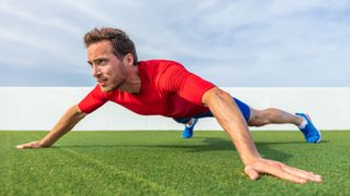 Man outdoors on grass performing an X plank with arms and feet wide