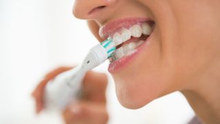 A woman brushing her teeth with an electric toothbrush