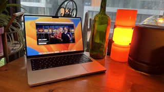 A 2023 14-inch MacBook Pro on a wooden counter, near a retro lamp.