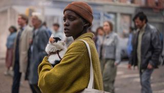 a woman in a yellow sweater and beanie holds a cat