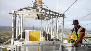 a large basket with a person beside in a reflective vest. behind is a landscape indicating they are quite a distance above the ground