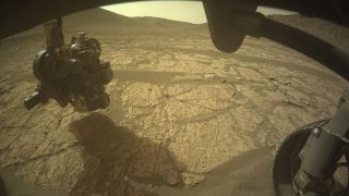 closeup of a mars rover's robotic arm investigating a patch of red planet ground