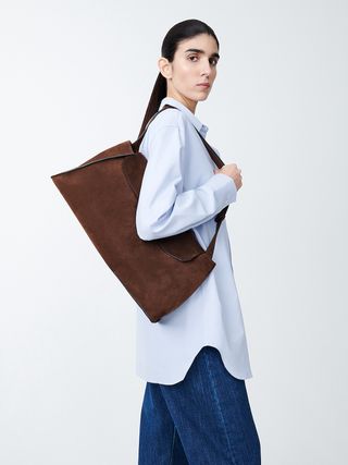 Woman wearing shirt and jeans holding Studio Nicholson suede bag