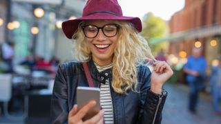 A woman looking at her phone while out in public, smiling widely and laughing