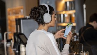 A woman wearing the Sony WH-1000XM5 headphones while using her phone in a cafe.