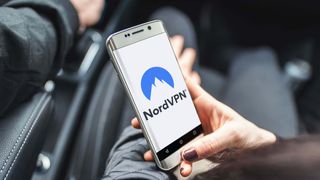 A hand holds a smartphone displaying the NordVPN logo