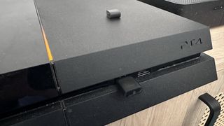 A Playstation 4 on a TV counter with a Bluetooth adaptor connected to a USB port.