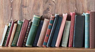 Old books leaning over on a wooden bookshelf