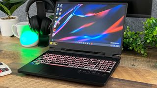 Bästa billiga gaminglaptop: En Acer Nitro 5 står öppnad på ett träfärgat skrivbord med en grön växt och ett headset på sidorna.