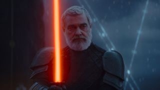 Still from a Star Wars movie. Here Baylan is holding a red lightsaber. He is an older adult male with short gray/white hair and a beard. He is wearing black armour. It is raining.