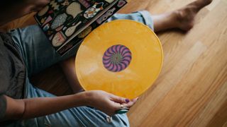 A yellow record being taken out of its sleeve by a man sitting on the floor